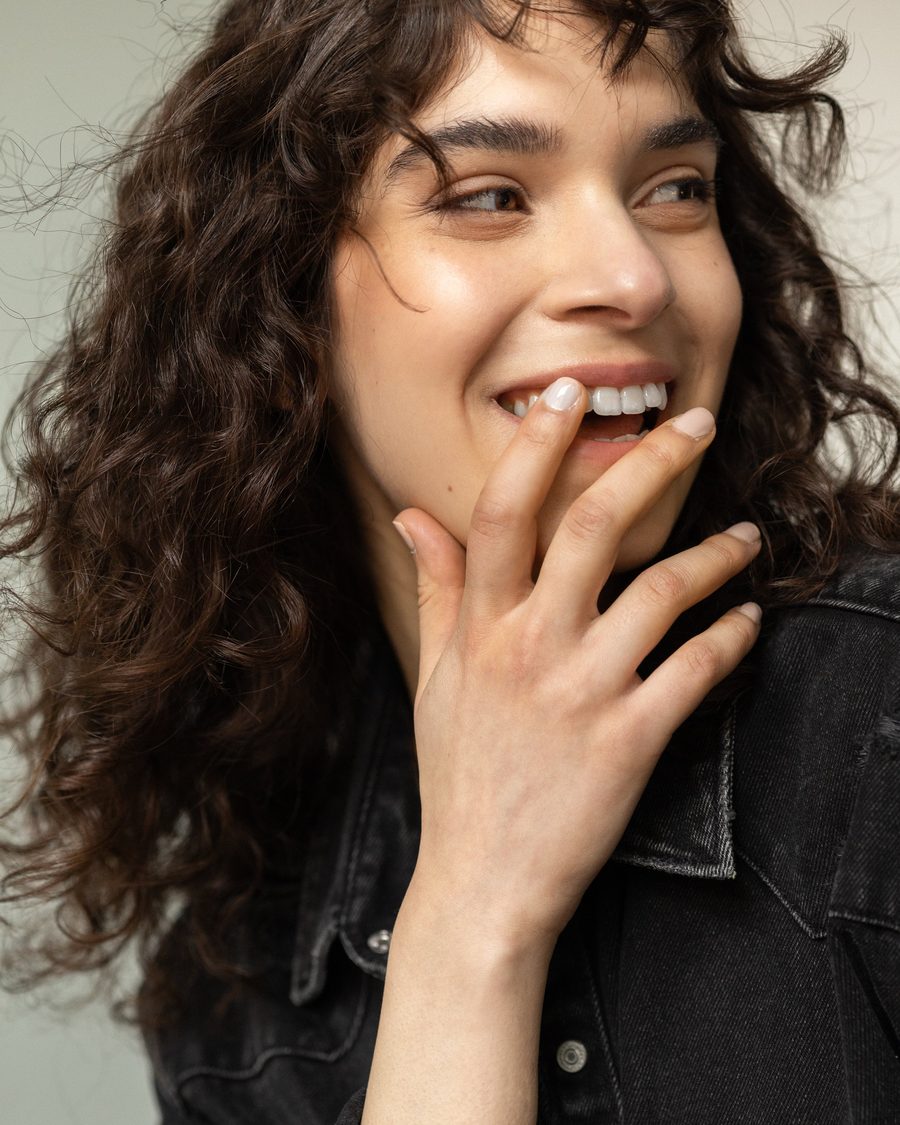 Woman with dark curls laughing, hand at her mouth