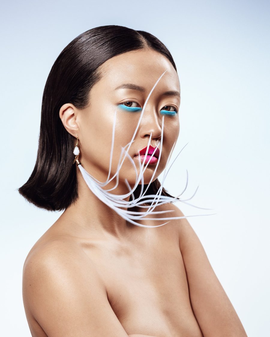 Portrait with turquoise eye make-up, pink lips and white feathers across the face