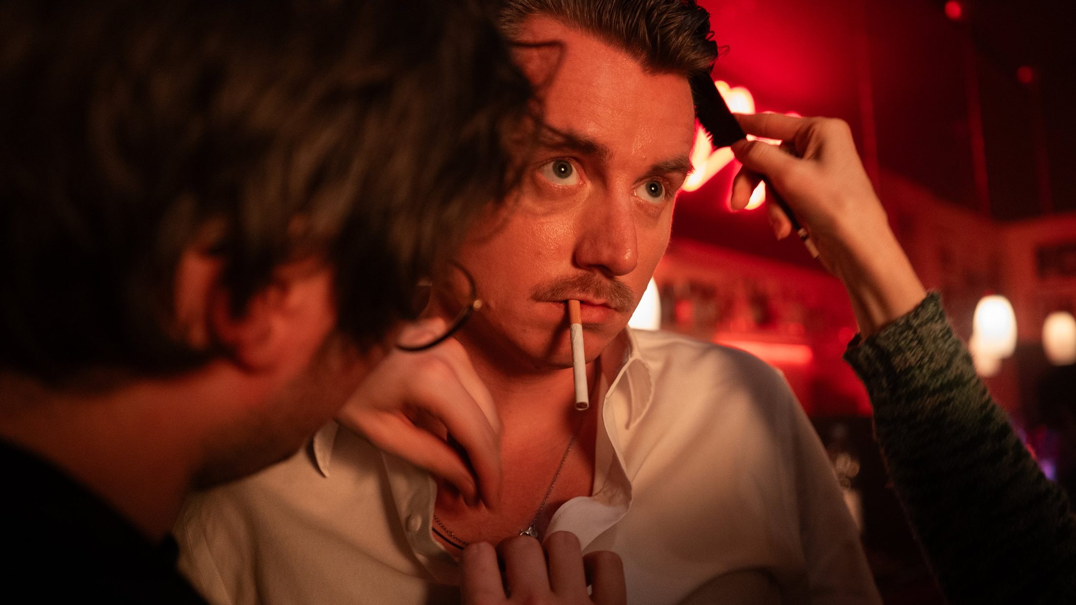 On set in a red-lit bar: an actor being touched up between takes