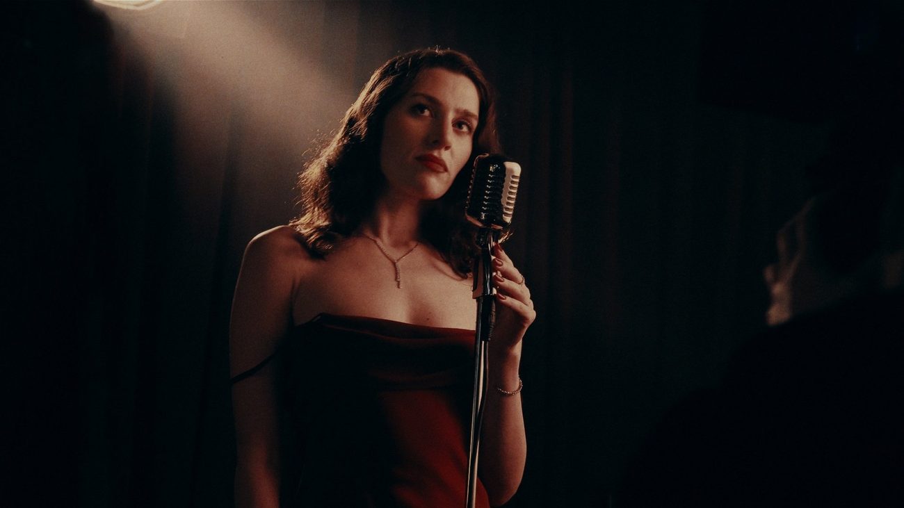Film still: a singer at a vintage microphone in a dark room