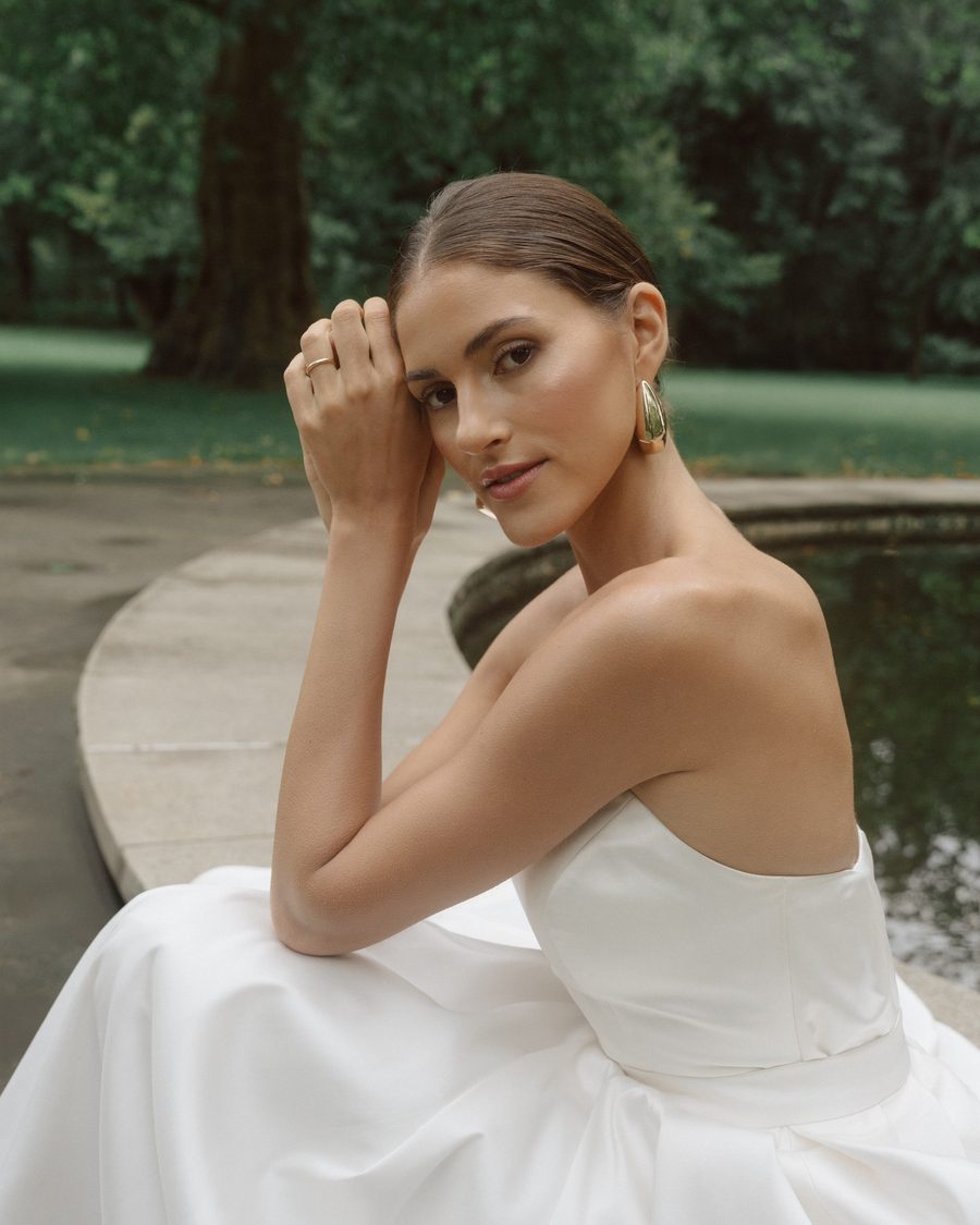 Bride in a strapless dress sitting by a fountain, hand at her forehead