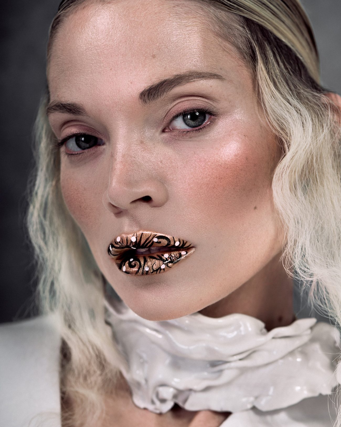 Close portrait, lips covered in gold leaf, white sculpted collar