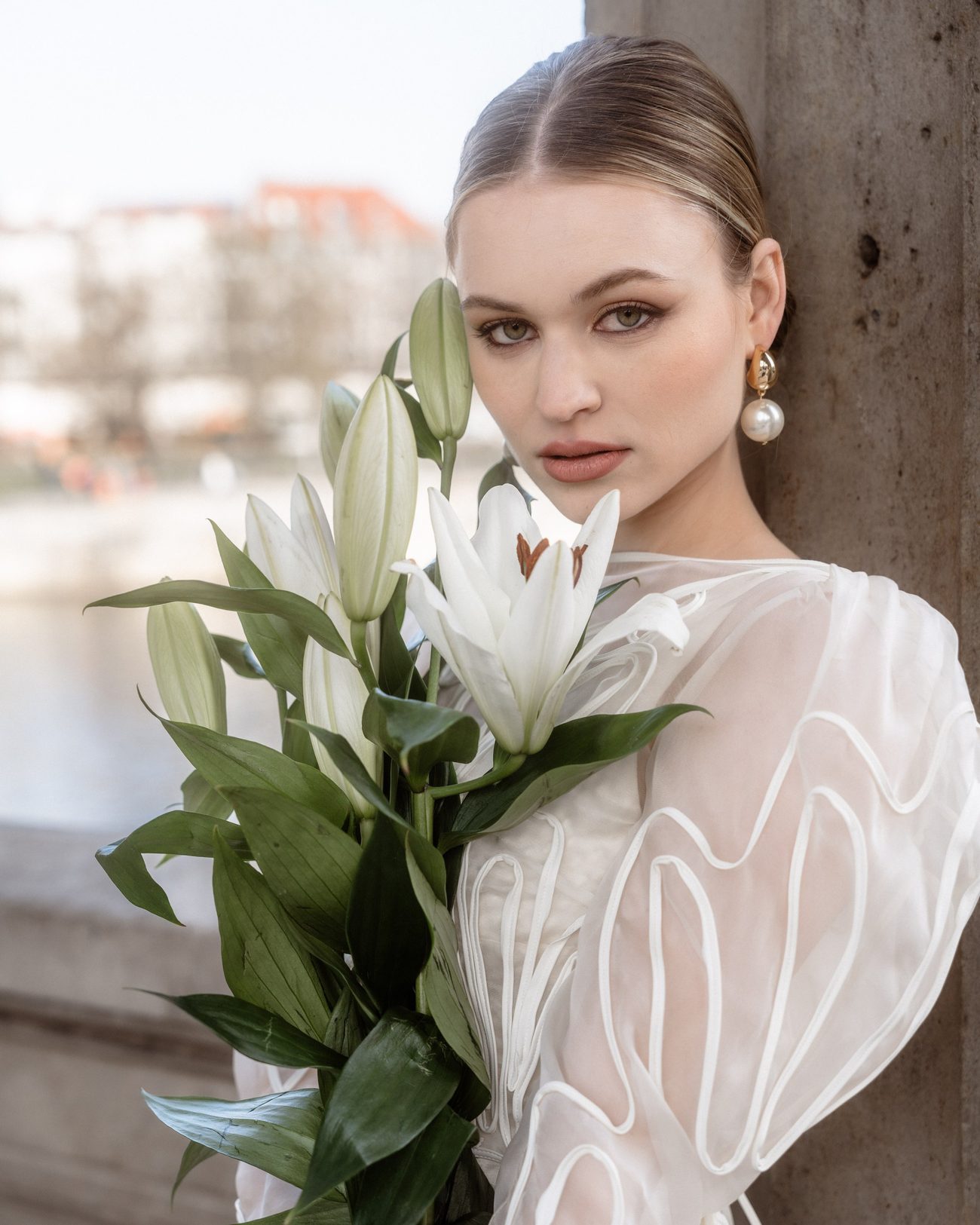 Bride holding white lilies, hair pulled back, pearl earrings