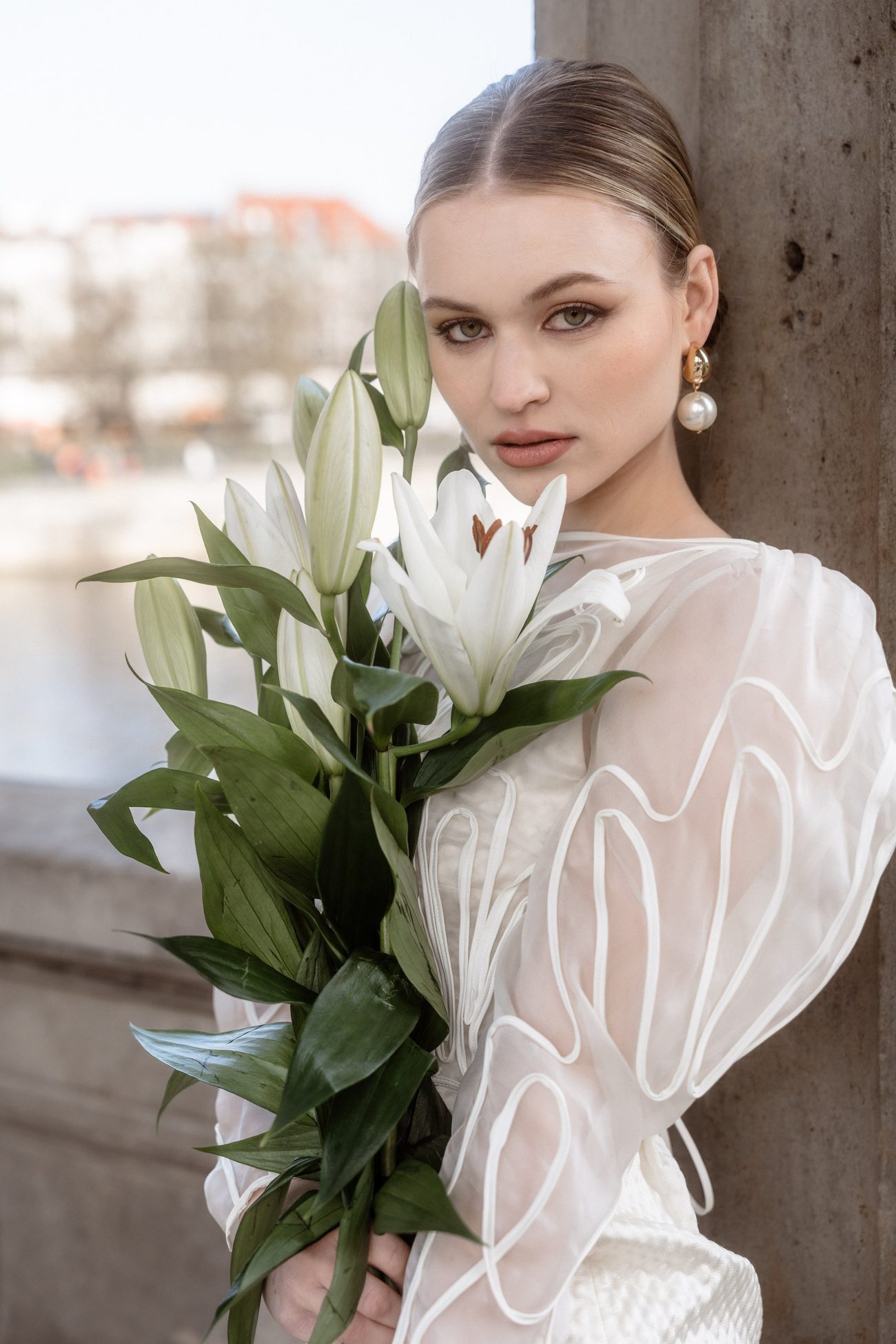 Bride holding white lilies, hair pulled back, pearl earrings