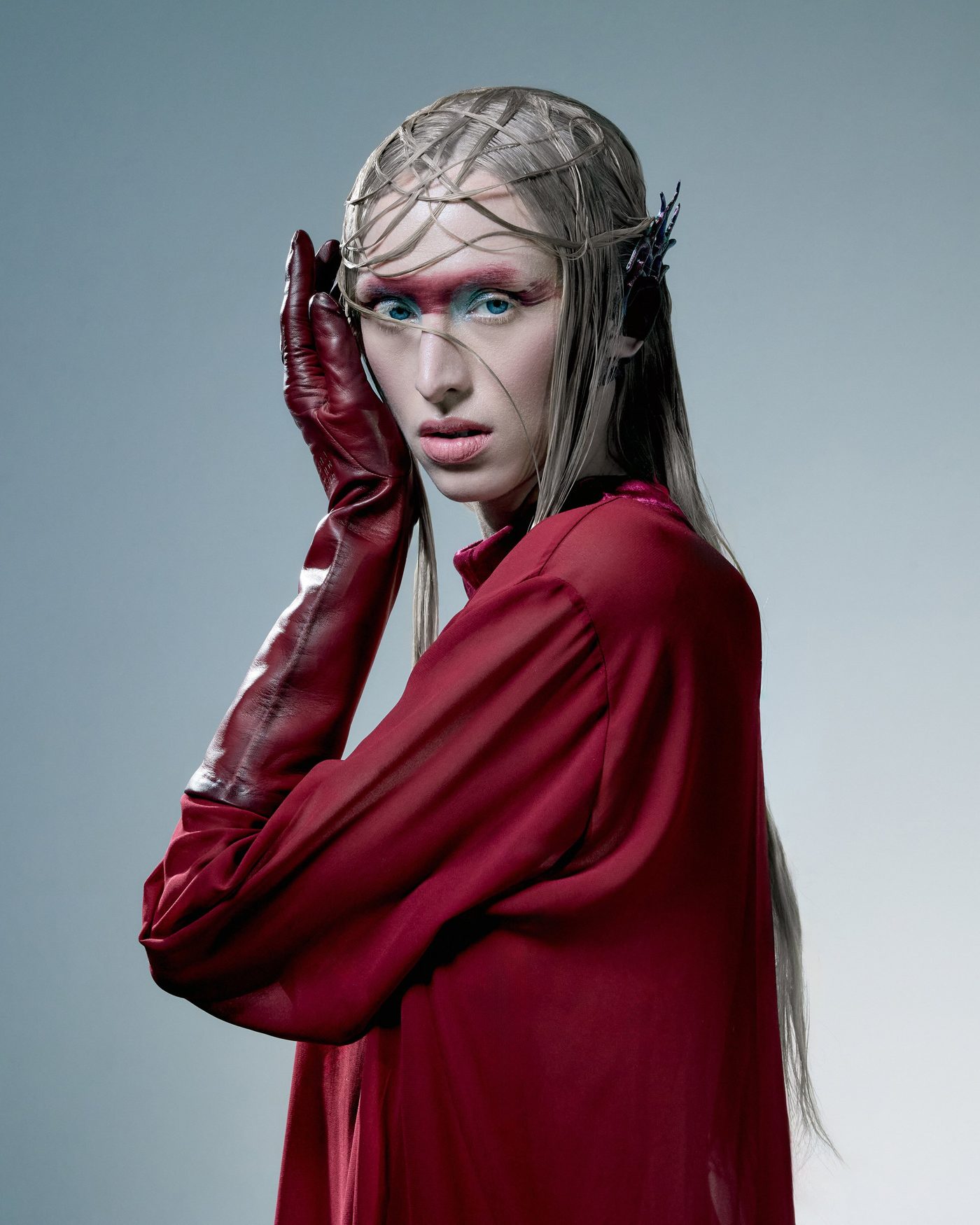 Woman in a red coat and red leather glove, red and blue eye make-up, a metal net over her hair