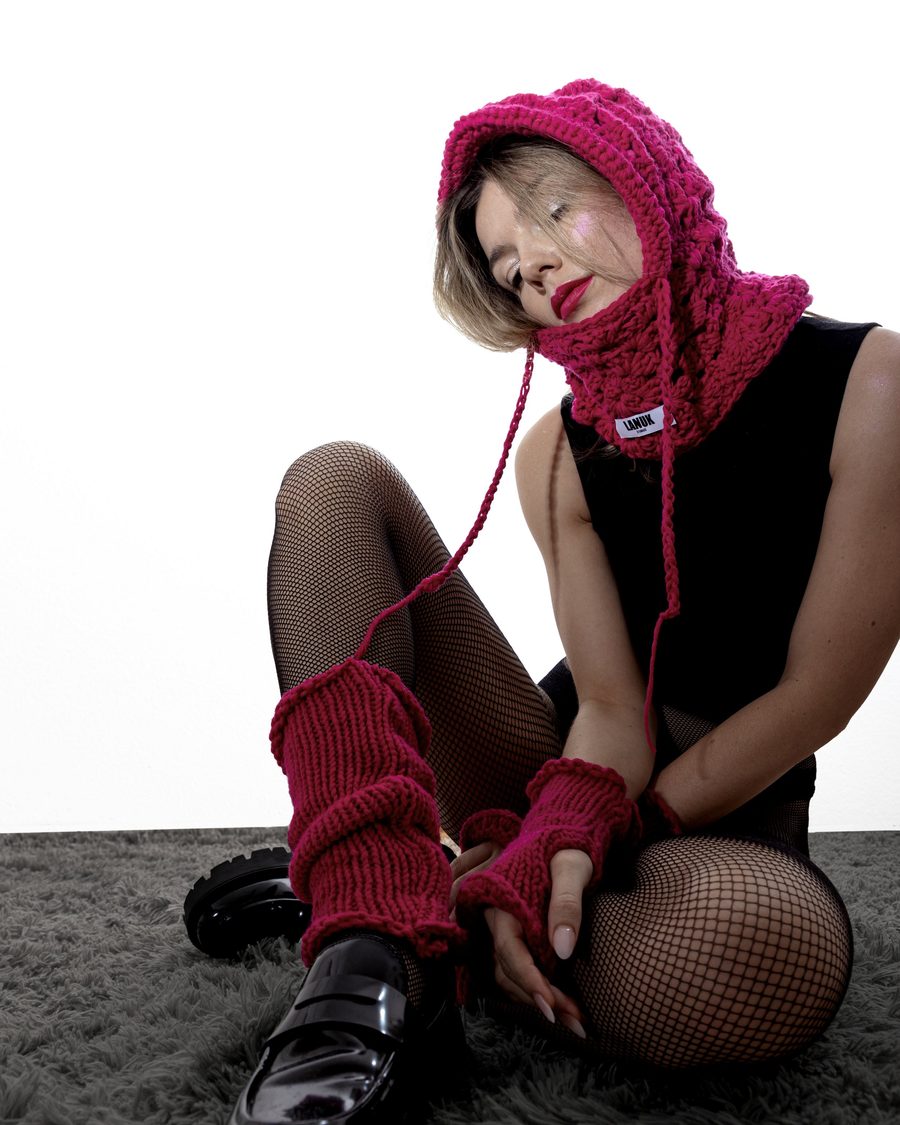 Model in a red knitted hood and gloves sitting on a grey rug