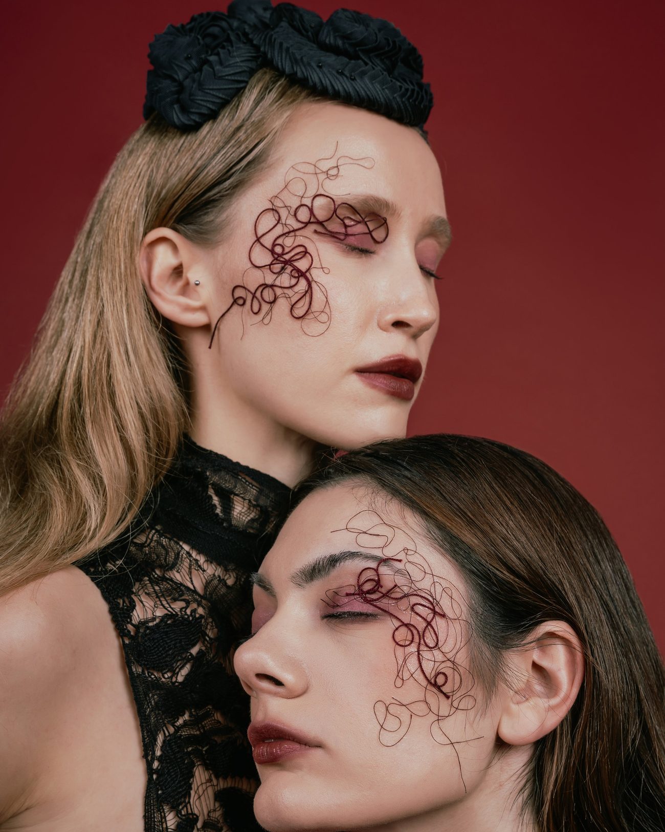 Two women against a red wall, fine red line drawings around the eyes