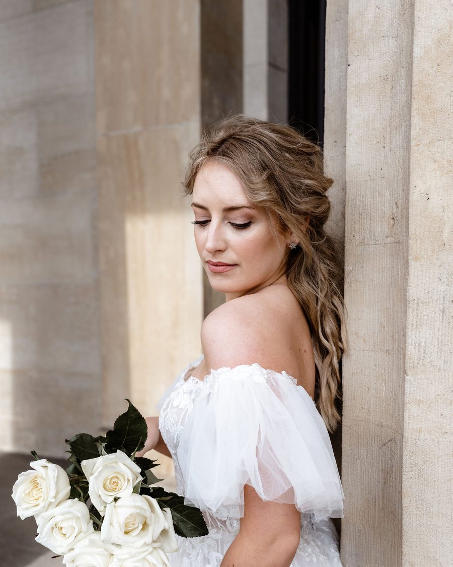 Bride with a long braid looking down at a bouquet of white roses